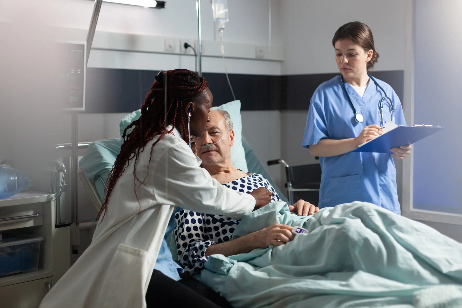 Two nurses helping a patient in a hospital bed
